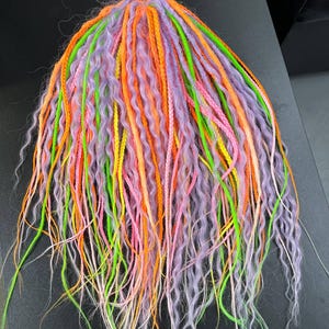 May include: A collection of vibrant synthetic dreadlocks in orange, purple, green, pink, and yellow. The dreads have a wavy texture and are arranged in a cascading style, suitable for alternative hairstyles.