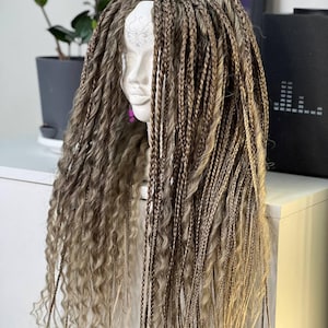 May include: A wig with long, braided, and wavy hair in shades of brown and blonde is displayed on a white mannequin head. The wig features a mix of tightly braided sections and loose, wavy strands, creating a textured and voluminous look.