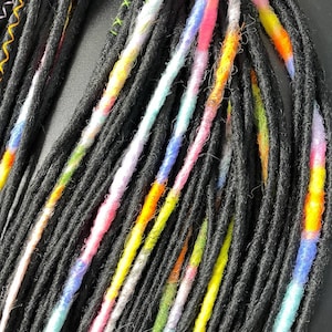 May include: Close-up of black dreadlocks with colorful accents. The dreads are a dark gray color, with sections of vibrant colors like pink, yellow, blue, and orange. Some dreads have decorative stitching in orange and green.