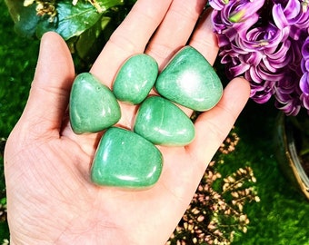 May include: Five smooth, green jade stones, tumbled and polished, in a hand. The stones are various sizes and shapes.