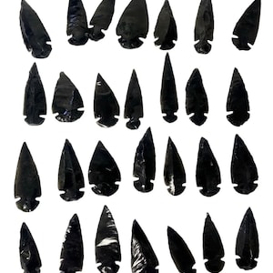 Puede incluir: Una colección de 28 puntas de flecha de obsidiana negra, cada una con una forma y un tamaño únicos. Las puntas de flecha están hechas de un material oscuro y brillante y tienen una punta afilada.