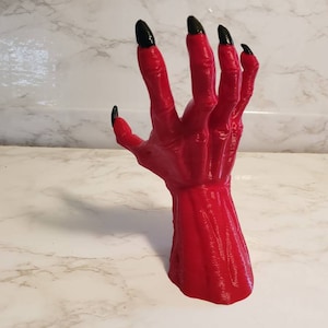 Könnte beinhalten: Eine rote, 3D-gedruckte Hand mit schwarzen Krallen, die nach oben ragt. Die Hand ist detailliert mit realistischer Muskeldefinition.