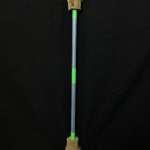 May include: A brown suede-like mop with a gray and green handle. The mop head is fringed and attached to the handle with a green band. The handle is gray with a green section in the middle. The mop is against a black background.