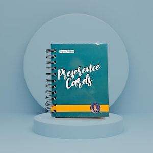 May include: A teal spiral-bound notebook with the words "Preference Cards" in white script. The notebook has a yellow stripe and a small circular sticker. The text "Surgical Tech Geek" is above the title.