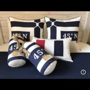May include: Nautical-themed decorative pillows and buoy-shaped accents in navy blue and white stripes. The pillows feature the text "45° N". The buoy accents have rope handles and patches.