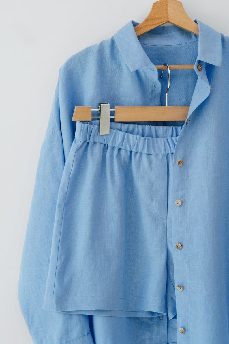 May include: A light blue linen shirt and shorts set. The shirt has a collar and button closure. The shorts have an elastic waistband.