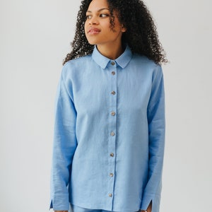 May include: A light blue linen shirt and shorts set. The shirt has a collared neckline and long sleeves. The shorts are a relaxed fit.