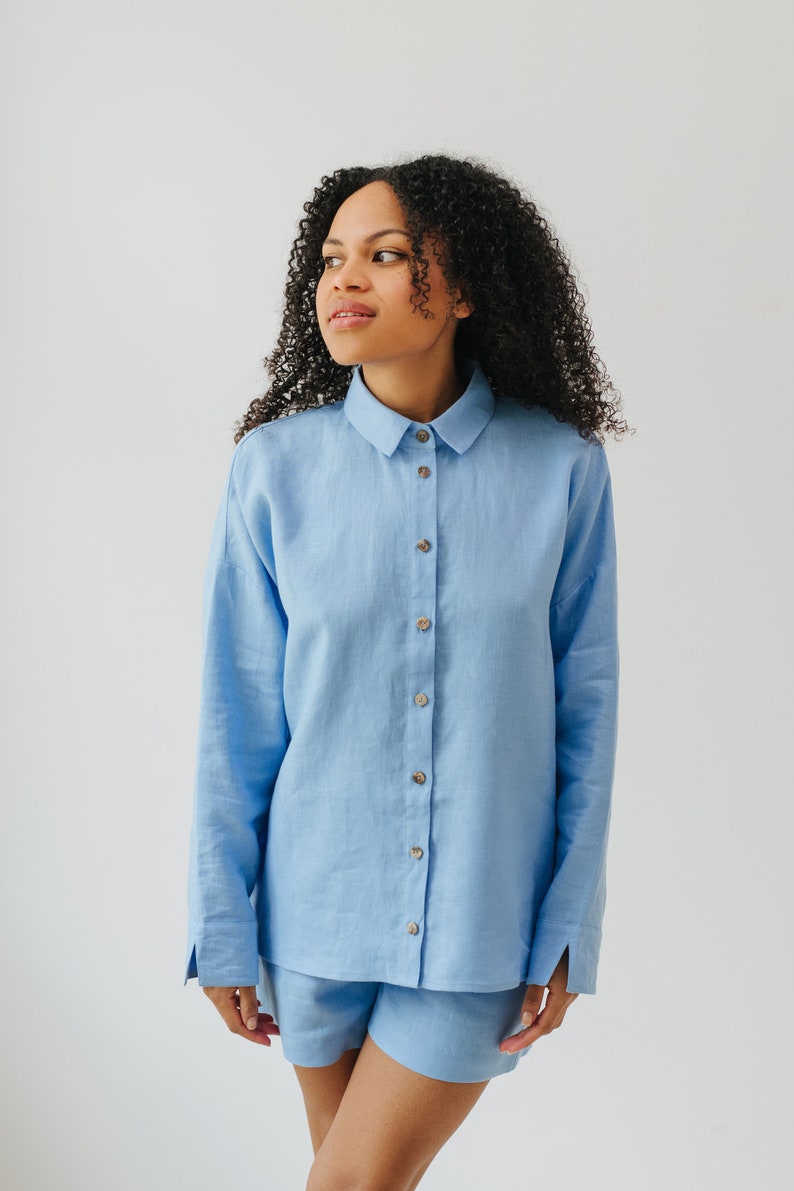 May include: A light blue linen shirt and shorts set. The shirt has a collared neckline and long sleeves. The shorts are a relaxed fit.
