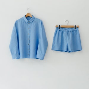 May include: A light blue linen shirt and matching shorts set. The shirt has a button-up front and long sleeves. The shorts have an elastic waistband.