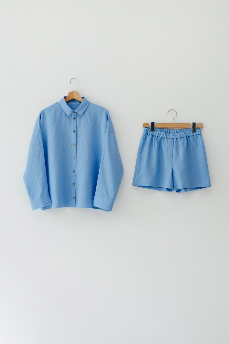 May include: A light blue linen shirt and matching shorts set. The shirt has a button-up front and long sleeves. The shorts have an elastic waistband.