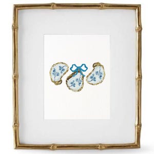 May include: Three blue and white oyster shells with a blue bow tied around the center shell. The shells are on a white background.