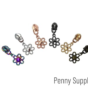 May include: Assortment of six metal zipper pulls in various colors, each featuring a flower-shaped design. The zipper pulls are in silver, gold, black, rainbow, and two shades of bronze.