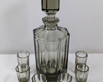 May include: A set of six gray glass shot glasses and a matching decanter with a faceted stopper.