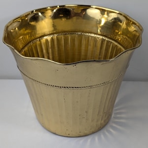 Puede incluir: Un macetero de metal dorado con un diseño acanalado y un borde festoneado.