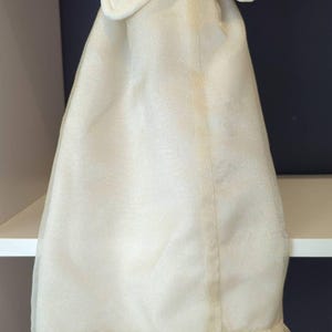 May include: Cream-coloured garment cover with a star-shaped top and a ruffled lace hem. The cover is made of a sheer, flowing fabric. The top has a padded, star-shaped design. The bottom edge features a delicate lace trim.
