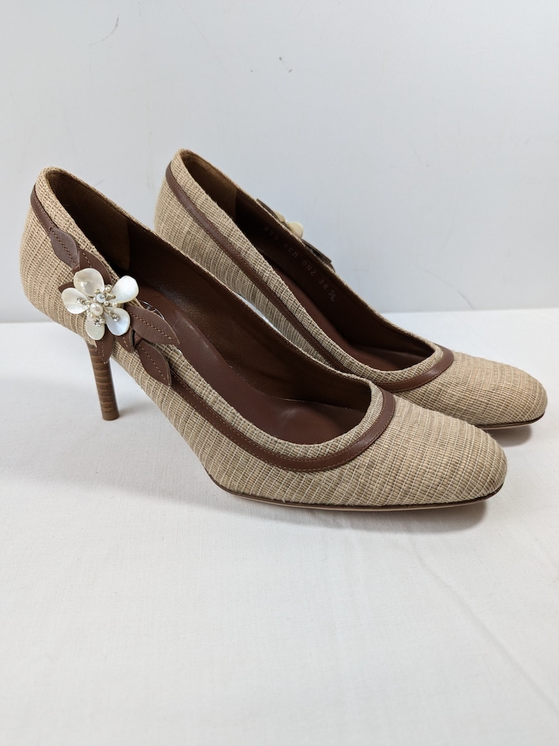 Puede incluir: Un par de zapatos de tac&oacute;n beige y marr&oacute;n con un adorno floral en la punta. Los zapatos est&aacute;n hechos de tejido tejido y tienen un ribete de cuero.