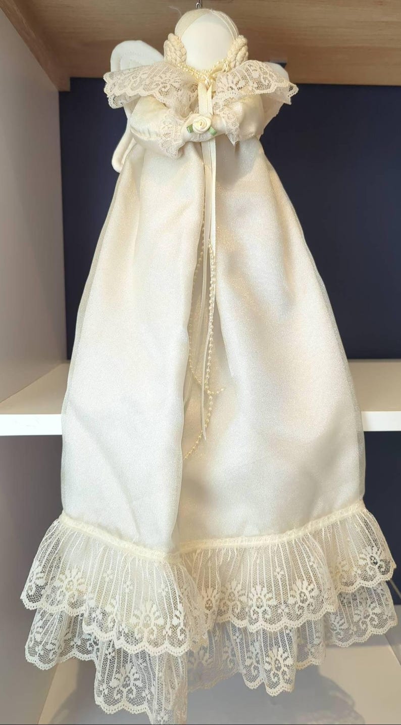 May include: Ivory angel doll with lace detailing. The doll features a pearl necklace and a small rose. The dress has a layered lace hem. The wings are visible behind the doll's head.