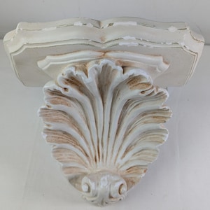 May include: White decorative shelf bracket with a scalloped design. The shelf bracket is made of plaster and has a distressed finish.