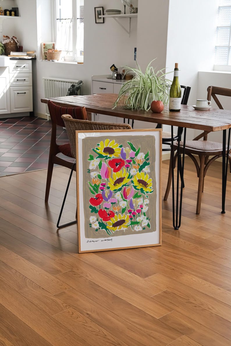 Op de afbeelding: Een ingelijste kunstprint met een kleurrijk bloemstuk met zonnebloemen en klaprozen. Het kunstwerk heeft een neutrale achtergrond en staat op een houten vloer. De tekst "flower market" is onderaan te zien.