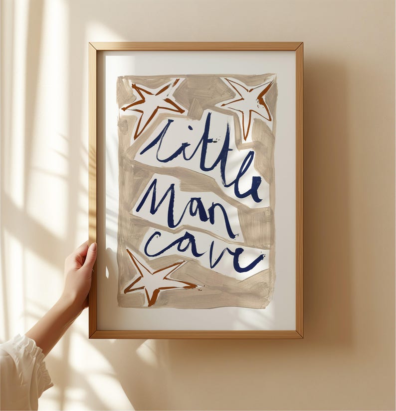 Op de afbeelding: Een ingelijst afdruk met een beige achtergrond en blauwe tekst die "little man cave" luidt. De afdruk bevat drie bruine sterren.