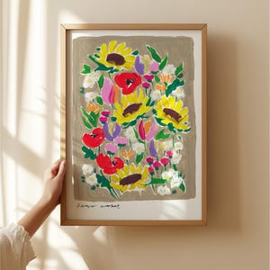 Op de afbeelding: Een ingelijste kunstdruk met een kleurrijk bloemarrangement, waaronder zonnebloemen en rode klaprozen, tegen een neutrale achtergrond. De print is gesigneerd met "Flower Market". De lijst is lichtbruin van kleur.