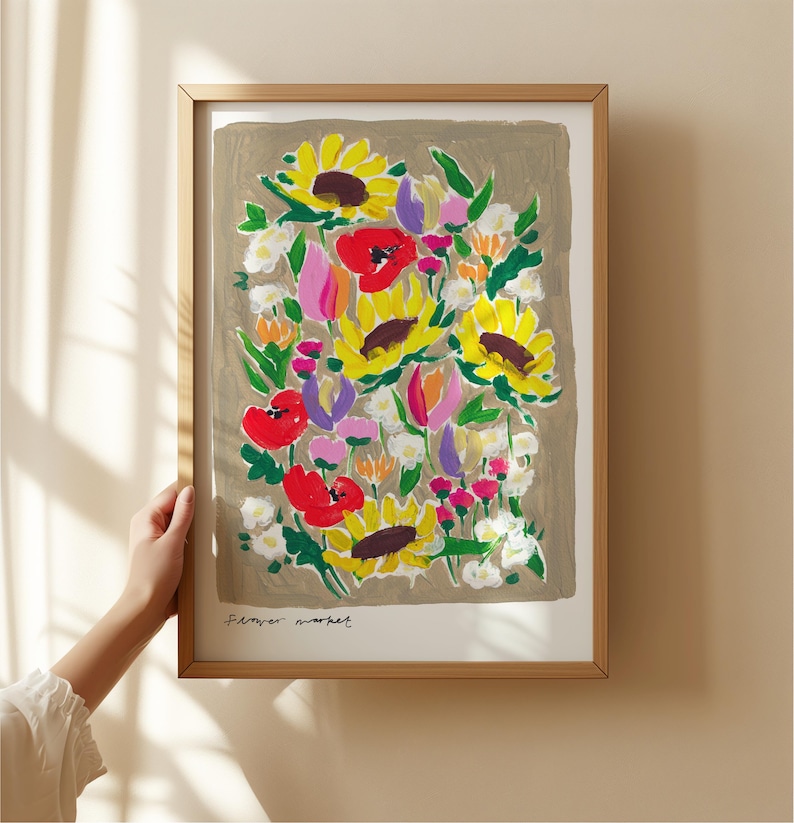 Op de afbeelding: Een ingelijste kunstdruk met een kleurrijk bloemarrangement, waaronder zonnebloemen en rode klaprozen, tegen een neutrale achtergrond. De print is gesigneerd met "Flower Market". De lijst is lichtbruin van kleur.