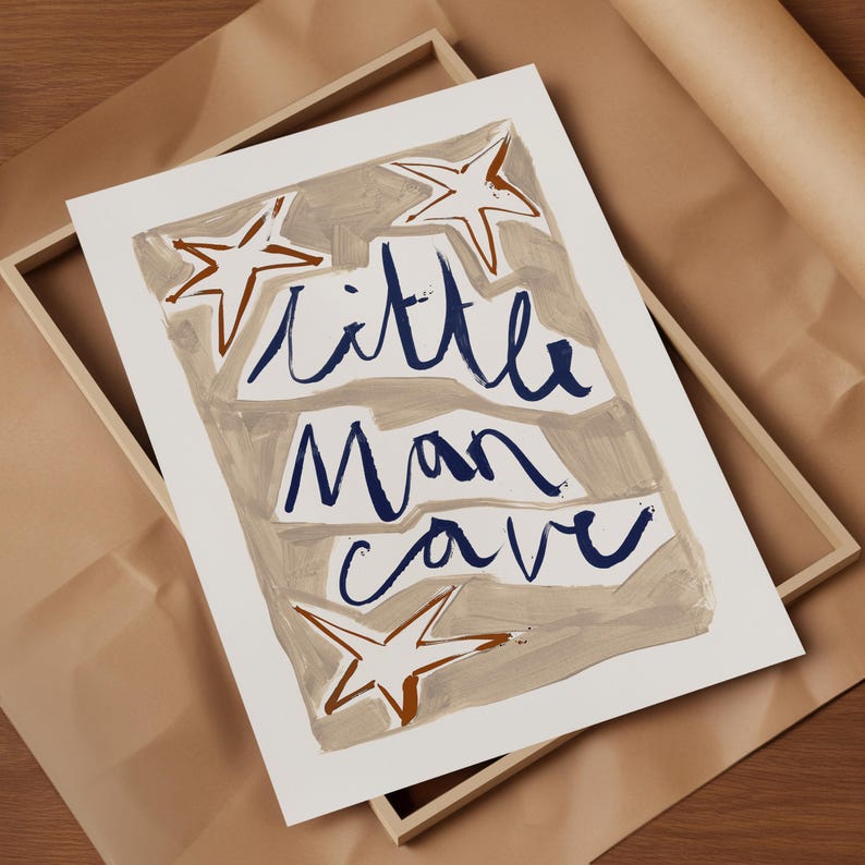 Op de afbeelding: Een witte print met de tekst "little man cave" in blauwe cursieve letters. De achtergrond is lichtbruin met drie witte sterren met bruine contouren.
