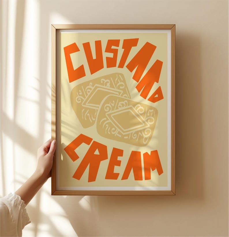 May include: A framed print with a yellow background and orange text that reads "Custard Cream". The print features a stylized illustration of two custard cream biscuits.