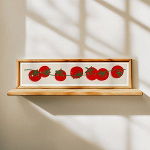 May include: A rectangular wooden framed print showing a row of red tomatoes with green stems on a beige background. The tomatoes are painted in a loose, brushstroke style. The print is displayed on a wooden shelf.