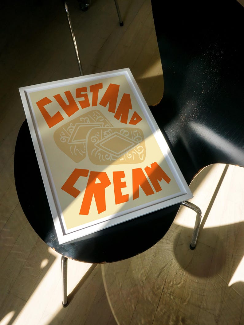 May include: A framed print with a white background and orange text that reads "Custard Cream". The image features three custard cream biscuits.