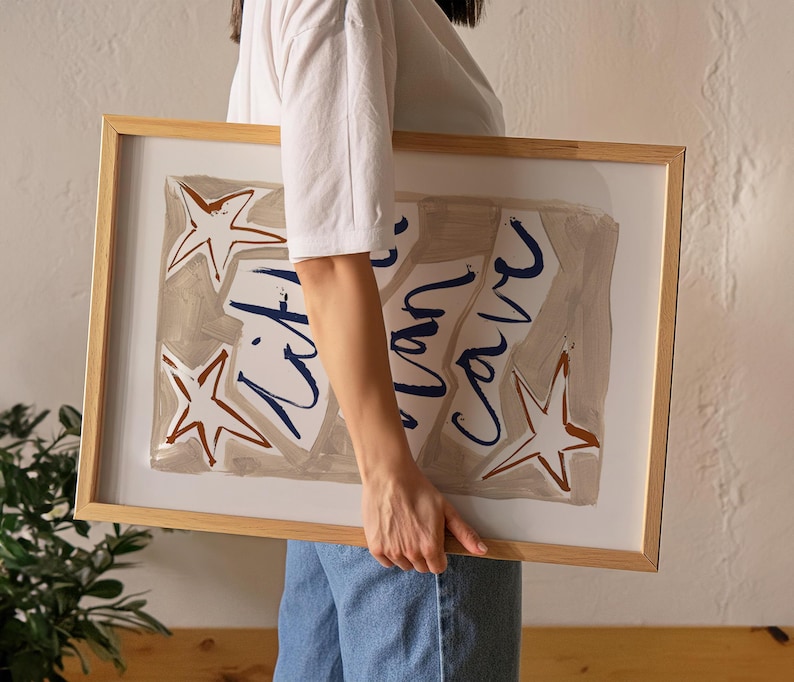 Op de afbeelding: Een ingelijst drukwerk met een beige achtergrond en blauwe en bruine abstracte vormen. De print bevat de tekst "life is now" en verschillende sterren.
