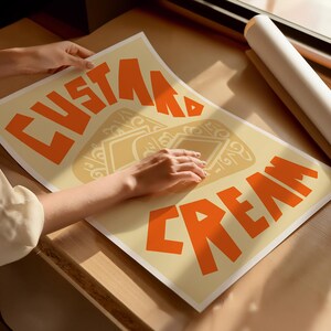 May include: A beige poster with the text "Custom Cream" in orange letters. The poster has a stylized design of a scoop of ice cream with a swirl of cream on top.