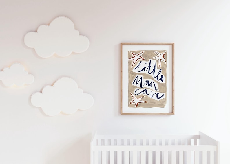 Op de afbeelding: Een ingelijst print met een beige achtergrond en witte sterren. De tekst "little man cave" is geschreven in blauwe cursieve letters.