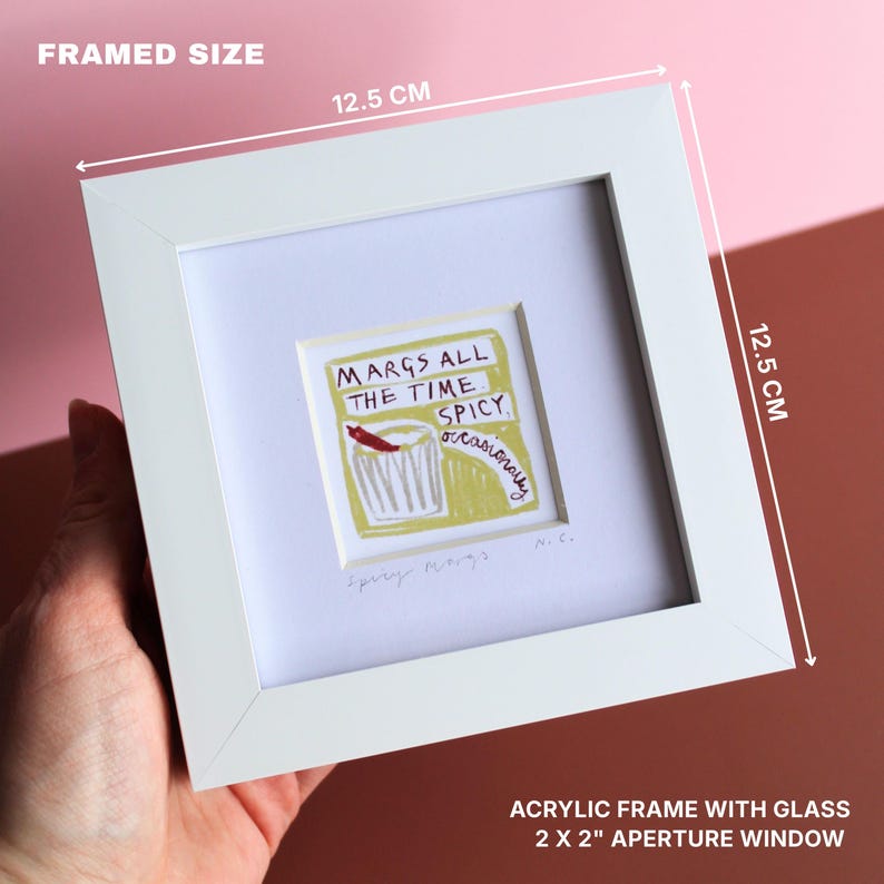 May include: A white framed art print with the text "MARGS ALL THE TIME SPICY occasionally". The print features a red chili pepper and a cocktail glass. The frame measures 12.5 cm x 12.5 cm, with a 2 x 2 inch aperture window.