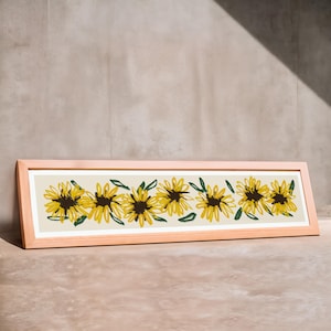 May include: A framed print of a row of yellow sunflowers with green leaves on a cream background. The frame is light wood.