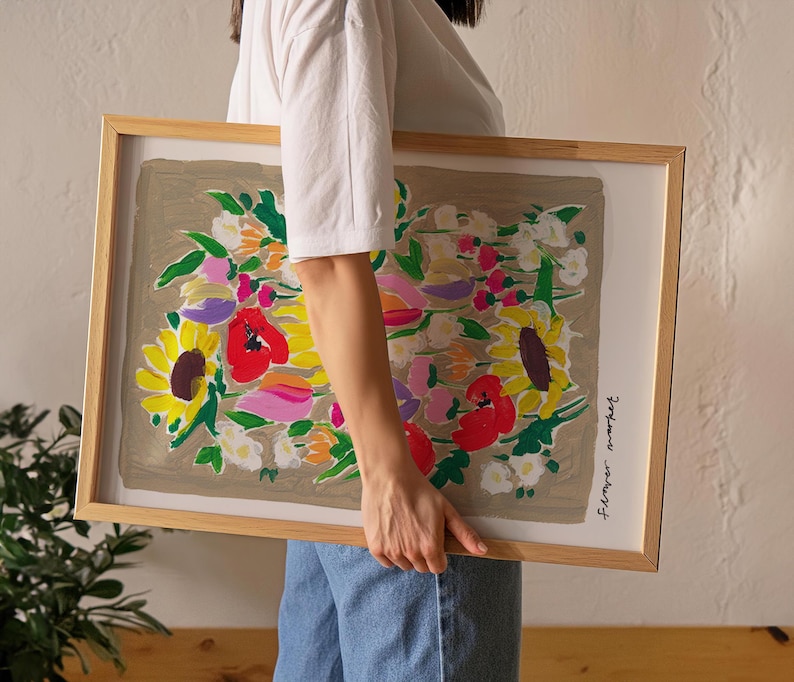 Op de afbeelding: Een ingelijste bloemenkunstprint met een boeket zonnebloemen, klaprozen en andere bloemen in geel, rood, roze en wit. Het kunstwerk is geplaatst tegen een neutrale achtergrond en ingelijst in licht hout.