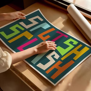 May include: A teal poster with the word "STITCH" in colorful, blocky letters. The letters are in shades of white, yellow, orange, pink, green, and blue. A rolled-up poster is visible in the background.