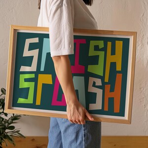 May include: A framed art print with the word "SPLASH" in colorful, bold, block letters. The letters are in white, light blue, pink, green, orange, and yellow against a teal background. The frame is made of light-colored wood.