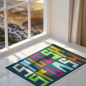 May include: A rectangular rug with a teal background and a colorful geometric design. The design features the word "STYLE" in white, orange, yellow, pink, and green block letters. The rug is placed in front of a window.