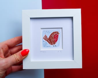 May include: A square white frame containing a small drawing of a brown robin with a red breast. The text reads: ROBINS APPEAR WHEN LOVED ONES ARE NEAR. The drawing is set against a light blue background with a white mat border inside the frame.