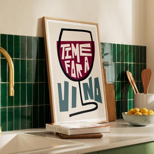May include: A framed print with a white background and a black outline of a wine glass filled with red wine. The text "TIME FOR A VINA" is written in the glass in a bold, colorful font.