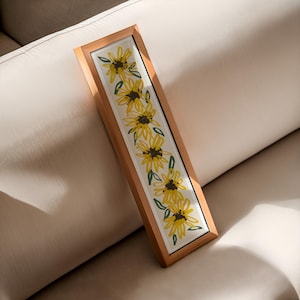 May include: A framed print of a vertical row of yellow sunflowers with green leaves on a white background. The frame is made of natural wood.