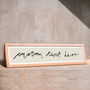 May include: A light wood frame with a beige background and black cursive text that reads "custom text here".