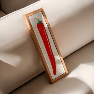 May include: A framed print of a red chili pepper on a white background. The frame is made of wood and has a natural finish.
