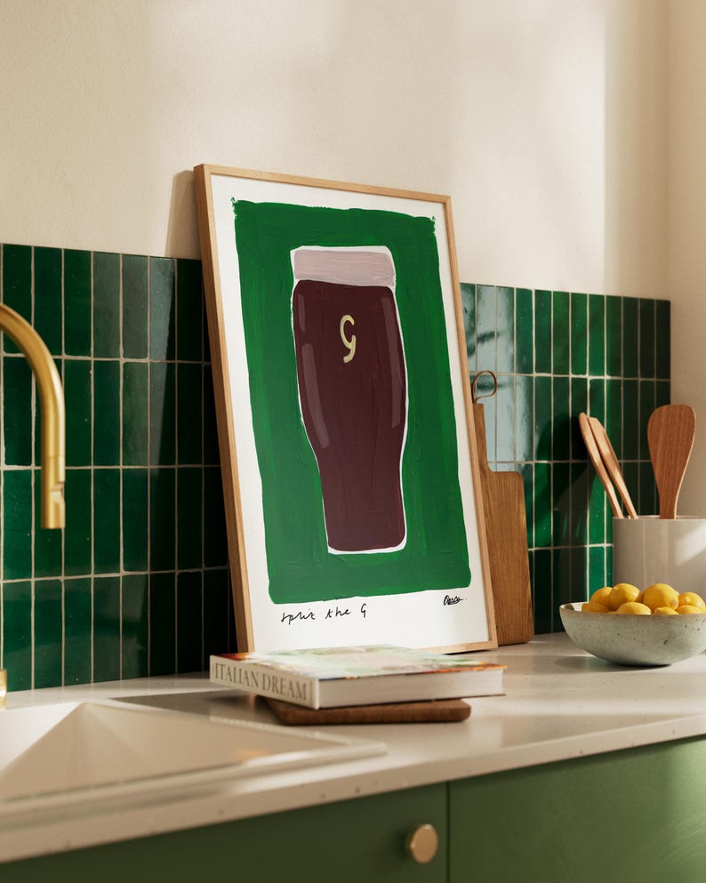 May include: A framed illustration of a pint glass of dark beer with the text "pour the g" and the artist's signature. The illustration is on a green background.