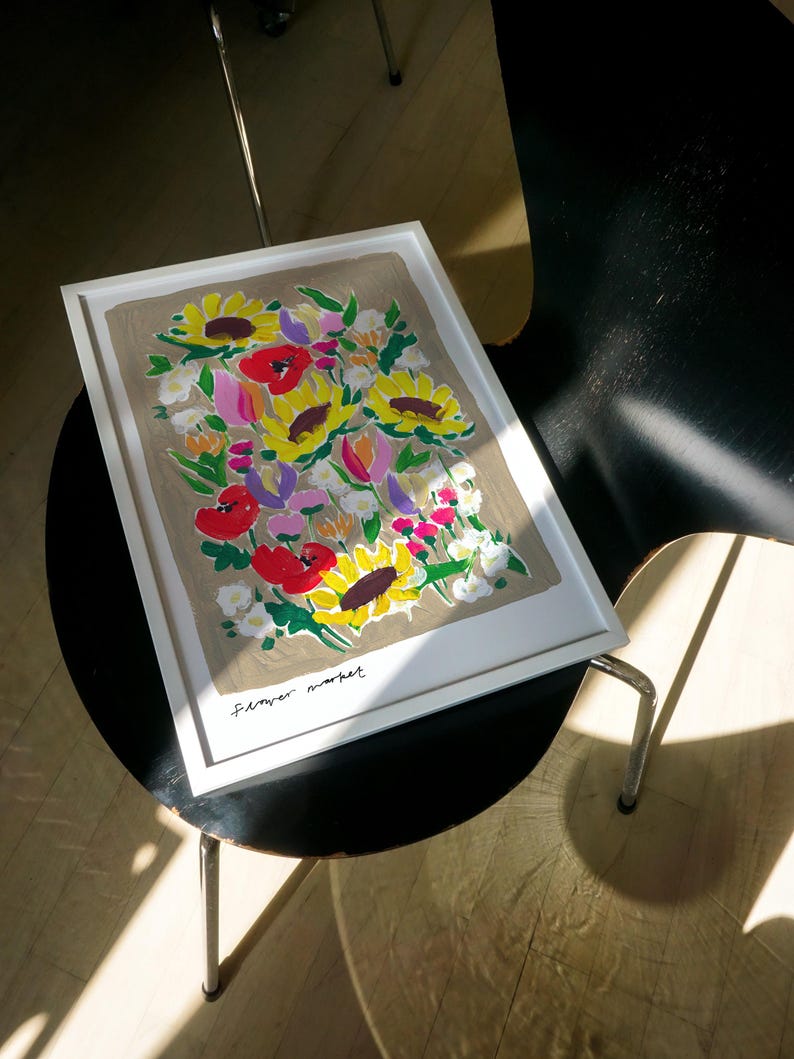 Op de afbeelding: Een ingelijste kunstdruk met een boeket zonnebloemen, rode klaprozen en andere kleurrijke bloemen. Het kunstwerk, gesigneerd met "Flower market", heeft een neutrale achtergrond en een witte lijst.