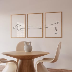 May include: Three framed black and white line drawings of a dachshund dog. The drawings are in a minimalist style and are hung on a white wall. The bottom drawing is signed "Picasso".
