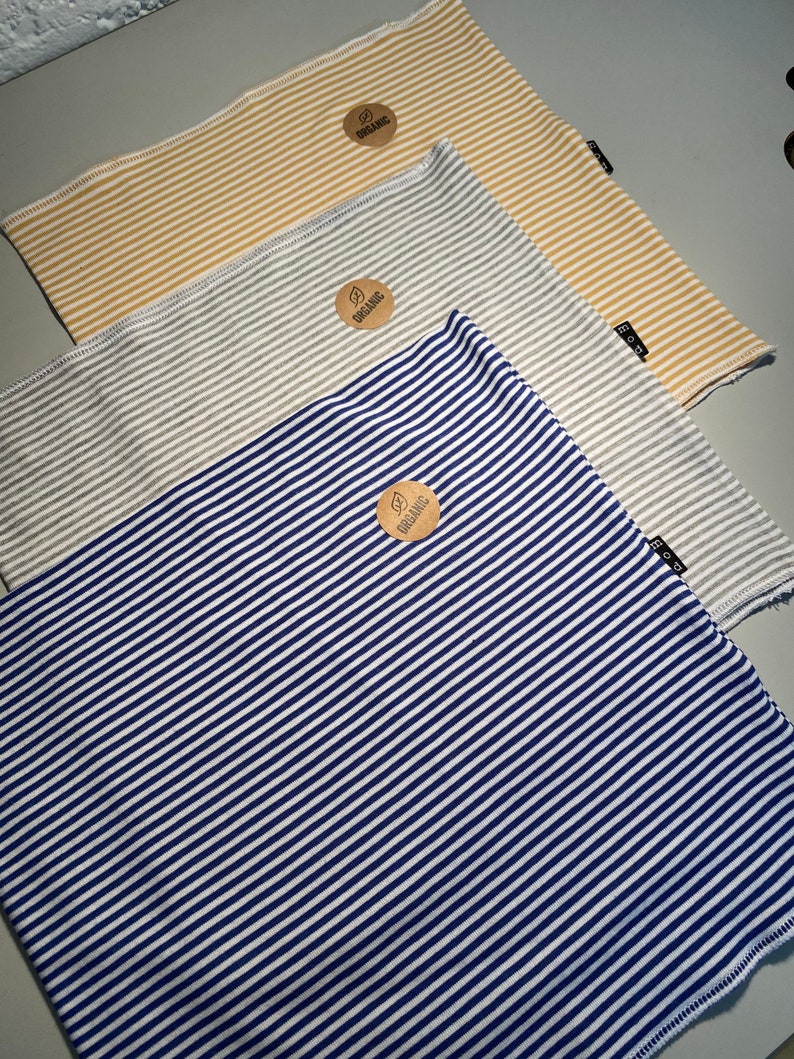 May include: Three striped fabric neck gaiters with a brown tag that says "organic" on each. The neck gaiters are yellow and white, gray and white, and blue and white.