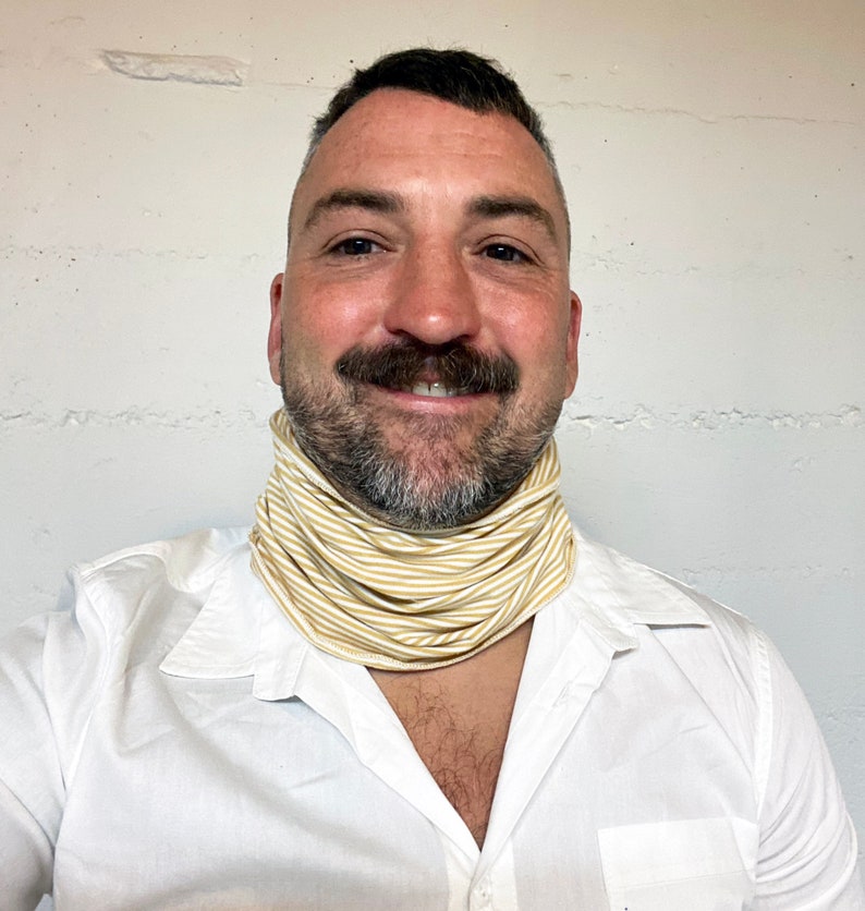 May include: A man wearing a white shirt with a yellow and white striped neck gaiter.