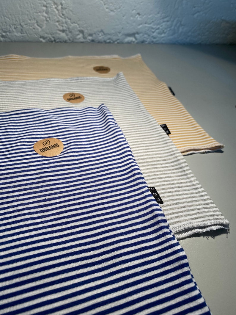 May include: Three striped fabric squares, one blue and white, one gray and white, and one beige and white. Each square has a small brown tag with the word "organic" printed on it.